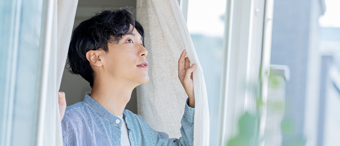 窓際のカーテンに触れる若い男性