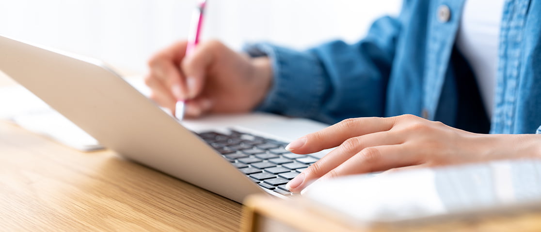 ノートパソコンを操作しながらメモを取る女性の手元
